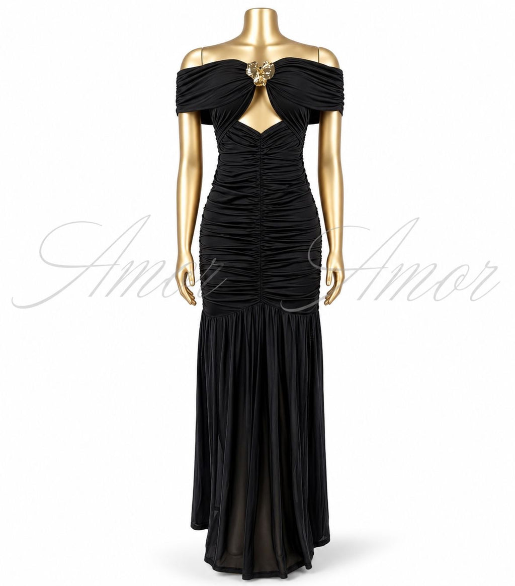Vestido largo disponible en color negro, rojo y blanco. Diseño con hombros descubiertos, detalle metálico al frente, fruncido que estiliza la silueta y abertura en pierna. Elegante y sofisticado.